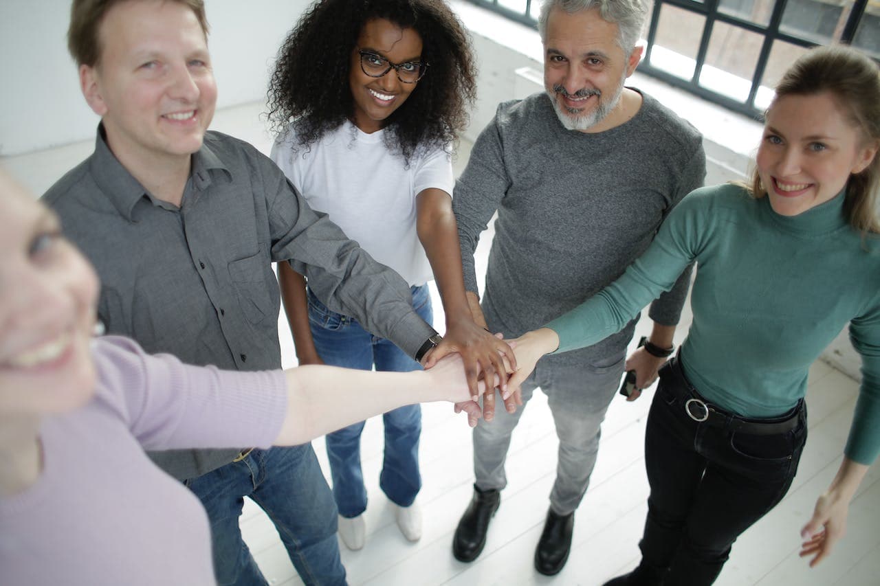 Happy diverse coworkers of different ages joining hands together in workspace