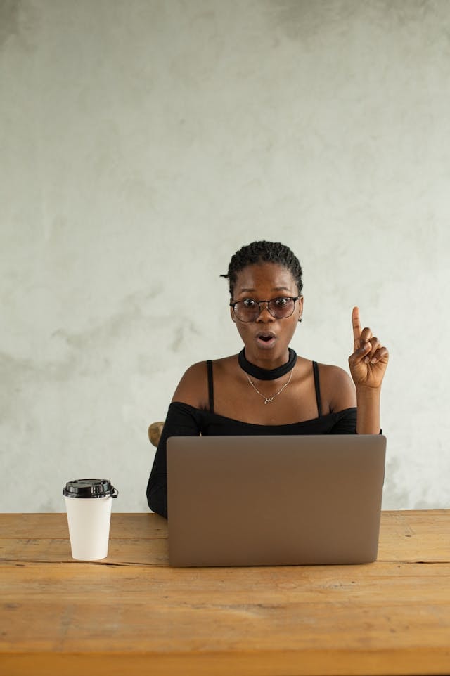 A person pointing her finger up while in front of a laptop