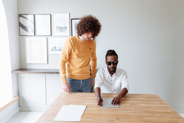 man-checking-the-person-writing-using-braille-slate-and-stylus