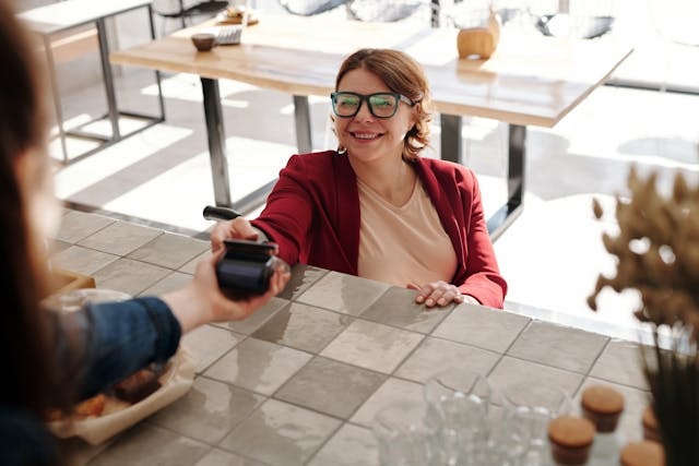 woman-in-red-blazer-holding-black-smartphone-paying-at-the-counter