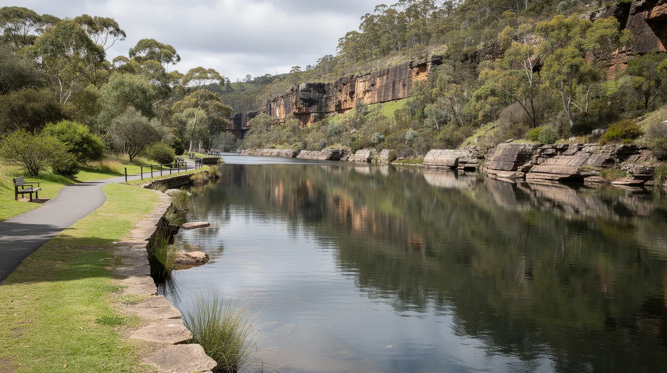 The image depicts the serene Cataract Gorge in Launceston, Tasmania, showcasing lush green walking paths and calm waters, all surrounded by vibrant trees. This tranquil setting highlights the importance of community participation and well-being, reflecting a perfect spot for individuals seeking emotional support and quality care through various NDIS services.